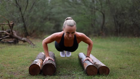 woman doing push-ups outdoors using logs for training