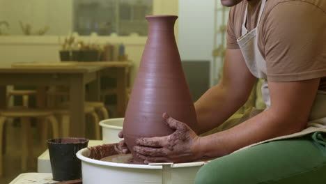 potter carefully cutting completed vase with thread on workshop pottery wheel