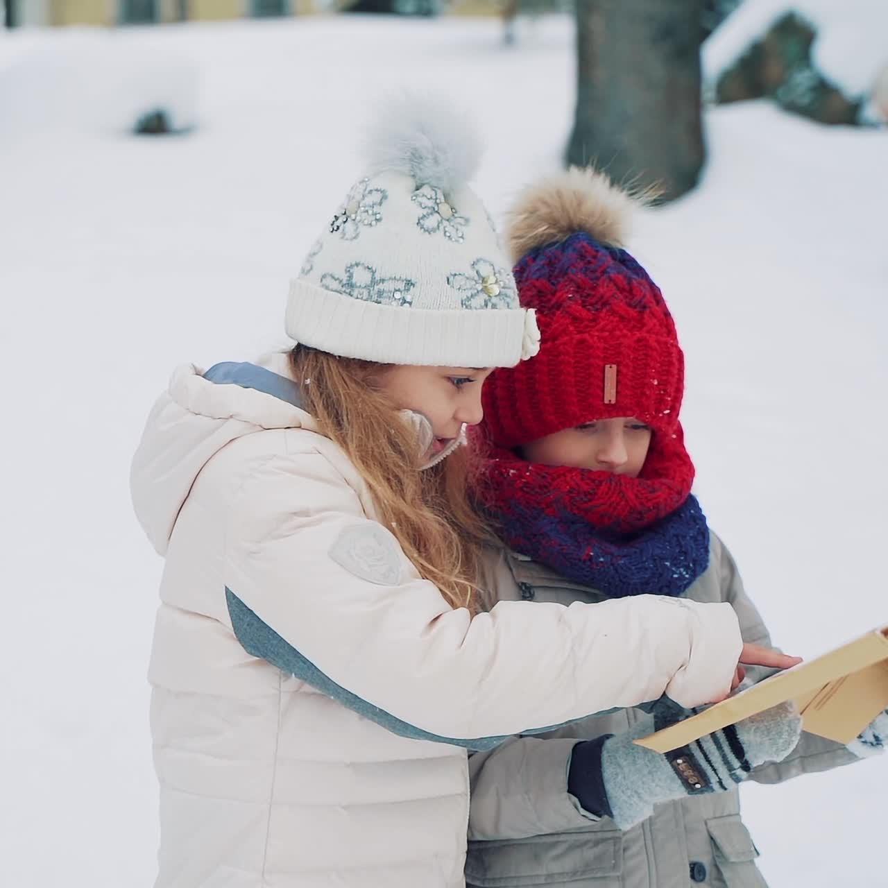 Cute kids are holding a large envelope in their hands and reading the address on it in the middle of the street in the winter. Chidren are looking for an address of home to give a letter. Slow motion. Blurred background