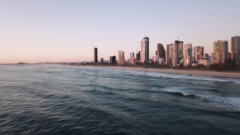 Toma-Aérea-Del-Amanecer-Con-Drones-Sobre-La-Playa-De-La-Ciudad-De-Surfistas-De-Remo-Atrapando-Olas