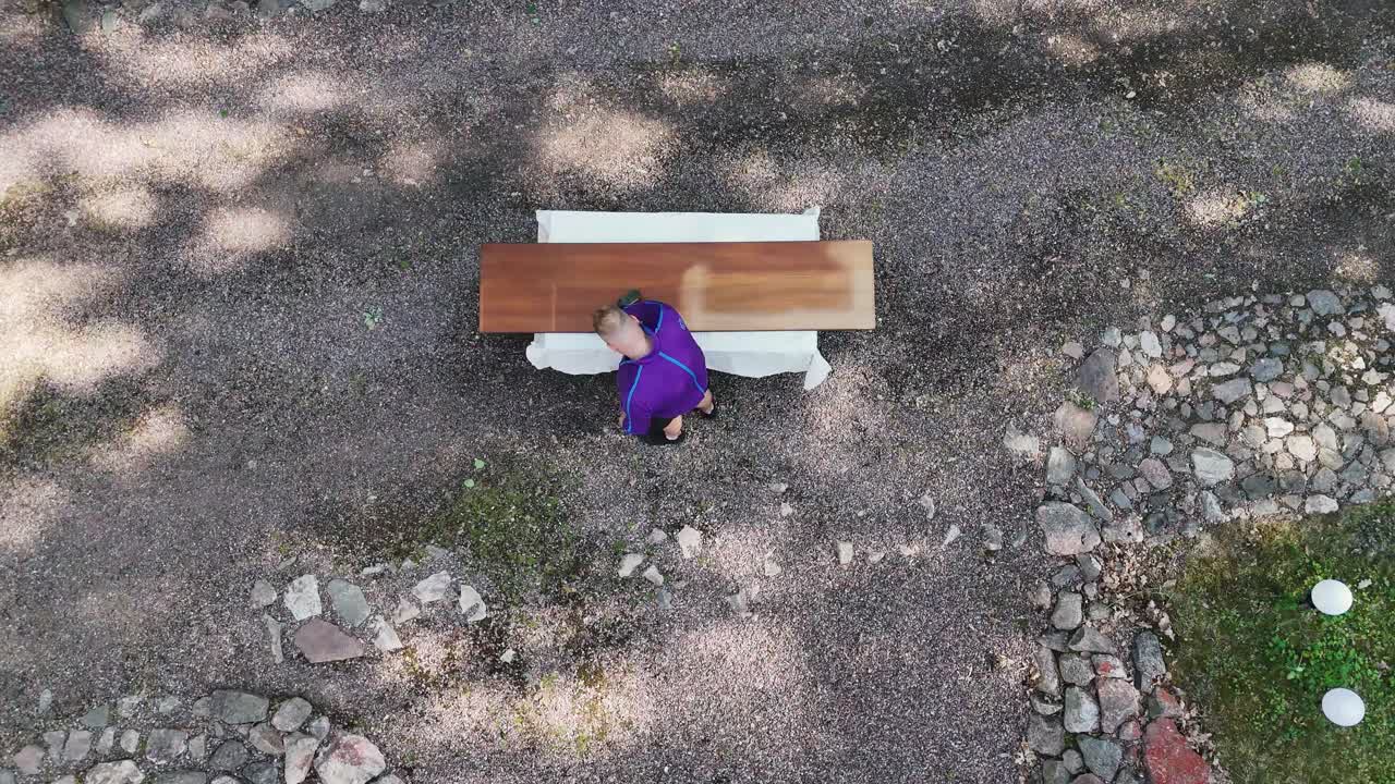 Person sanding wooden table in garden, top-down view, sunny day, aerial shot