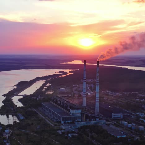 factory on colorful sky background at sunset. harmful smoke filling the air from industrial pipe in the evening. manufacturing near the river. aerial view.