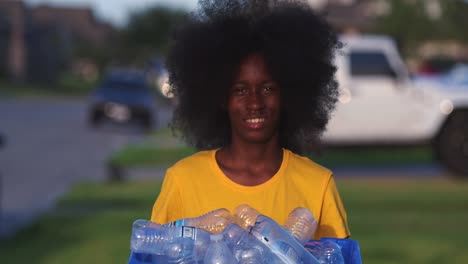 Adolescentes-Afroamericanos-Con-Una-Gran-Sonrisa-Afro-Mientras-Sostiene-Una-Papelera-De-Reciclaje-Llena-De-Botellas-De-Plástico