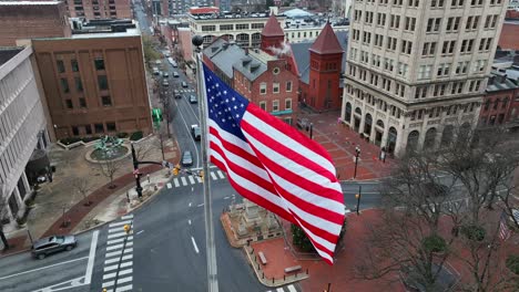 aerial establishing shot of american flag waving over city square during winter