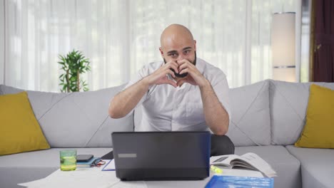 home office worker man makes heart symbol looking at camera.