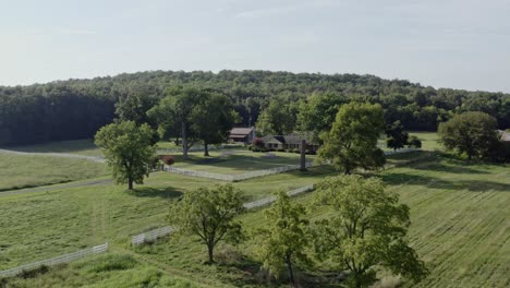 4K-aerial-pushing-in-from-field-on-small-farmhouse-surrounded-by-white-fence