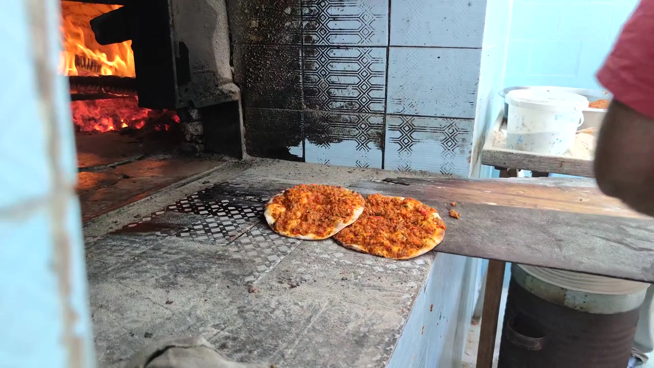 Baker Removing Fresh Lahmacun from Traditional Wood-Fired Oven