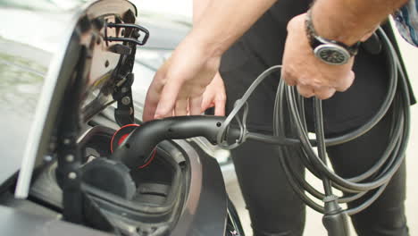 the hands of a man connecting one end of a cable to the battery of an electric car