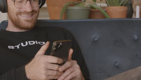 medium close front angle of a man sitting on a couch scrolling and swiping and typing on an iphone