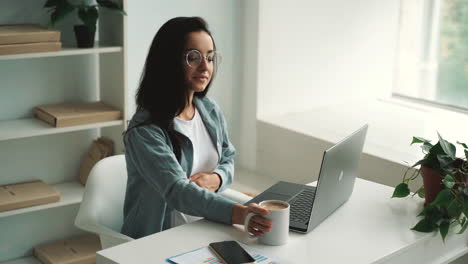 young pregnant business woman works using a laptop and takes a hot drink