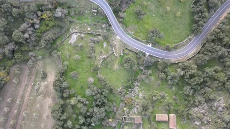 vuelo aéreo sobre un paisaje rural que mezcla una carretera, tierras de cultivo, restos de edificios antiguos y pequeñas áreas boscosas