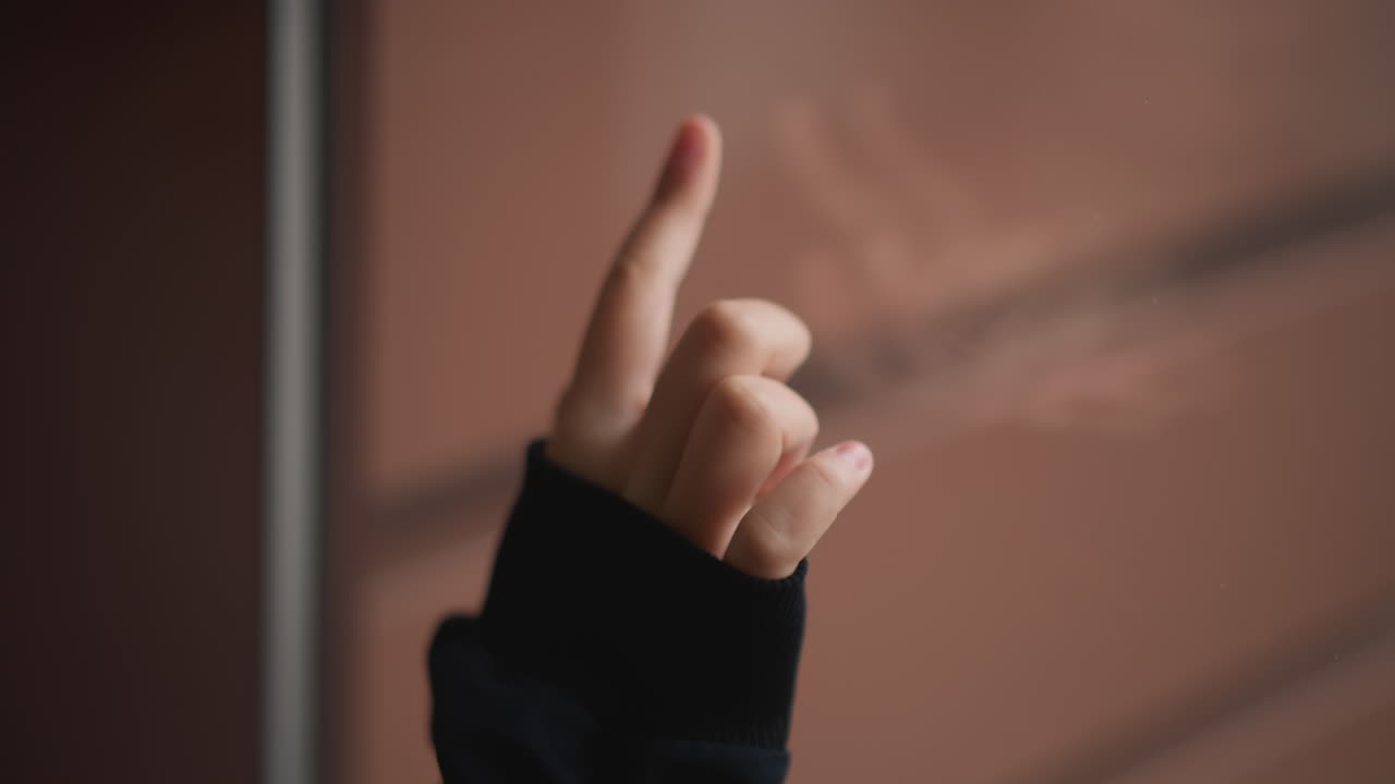 Palmo e polpastrello su vetro bagnato, primi piani intimi di una mano che preme e indica su un vetro appannato, tracciando gocce di pioggia e striature, lenti gesti tattili, focus sensoriale con toni smorzati, bambino che esplora.