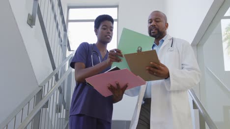 Médicos-Afroamericanos,-Hombres-Y-Mujeres,-Sosteniendo-El-Portapapeles-Y-Hablando-En-El-Hospital