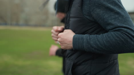 close-up of three people jogging on a track near a grassy field, with a clear view of the adult in the foreground and a blurred view of the other young boys in the background