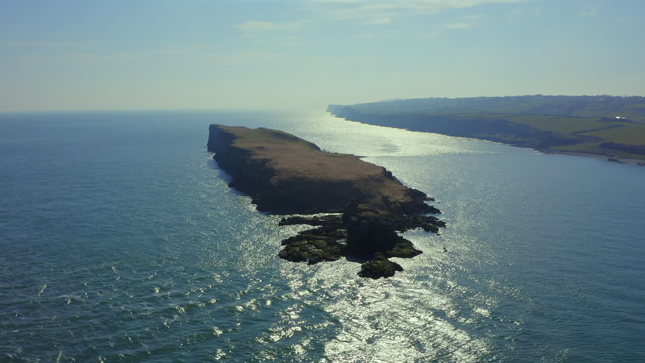 Wide aerial pullback rising over Portmuck Island on a clear, sunny day. Antrim, Northern ireland