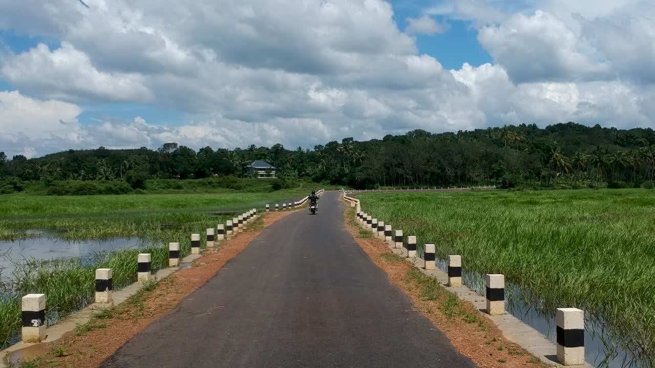 Motorbike rider riding a vintage bike,gut road,Indian road,road between water field,gut road
