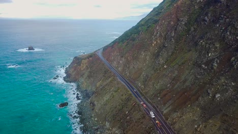Overhead-aerial-view-of-a-car-driving-along-cliffs-of-the-Pacific-Ocean-coast-in-Big-Sur-on-State-Route-1-in-California