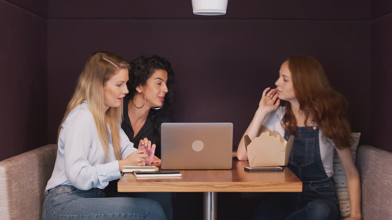 grupo de jóvenes mujeres de negocios sentadas alrededor de una mesa en un espacio de trabajo moderno teniendo una reunión de almuerzo de trabajo