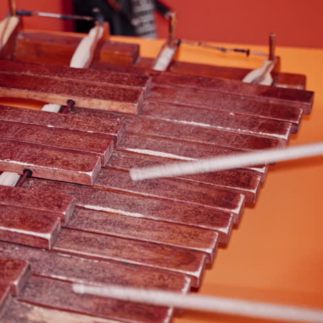 female hands holding sticks and playing the xylophone on the orange table. wooden instrument and woman plays with special sticks indoors. close-up.