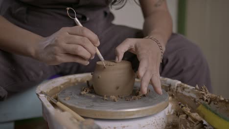 potter carefully uses cutting ribbon tool to refine clay pot on rotating wheel medium shot