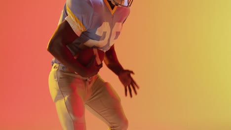 Video-of-african-american-american-football-player-with-ball-over-yellow-to-orange-background