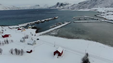 drone view in tromso area in winter flying over a snowy landscape surrounded by the sea and a frozen port with boats in norway