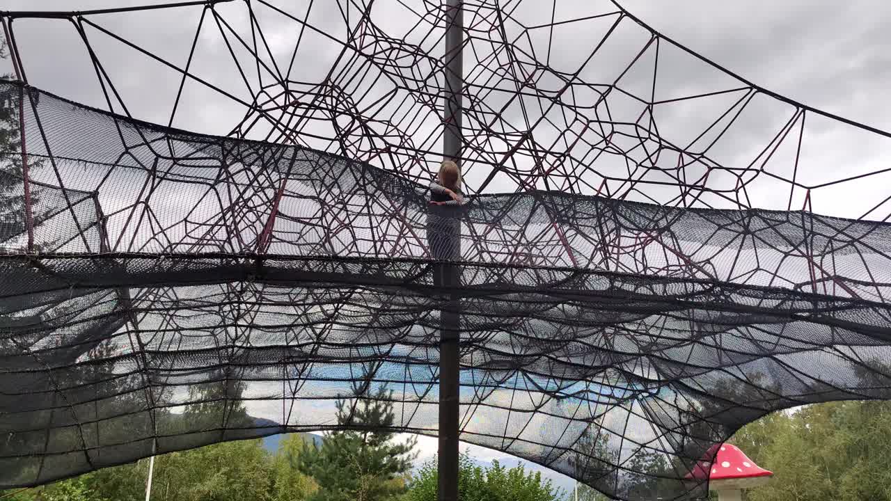 Female young child having fun all alone inside huge rope climbing tower at playground - Static film from below - Norway