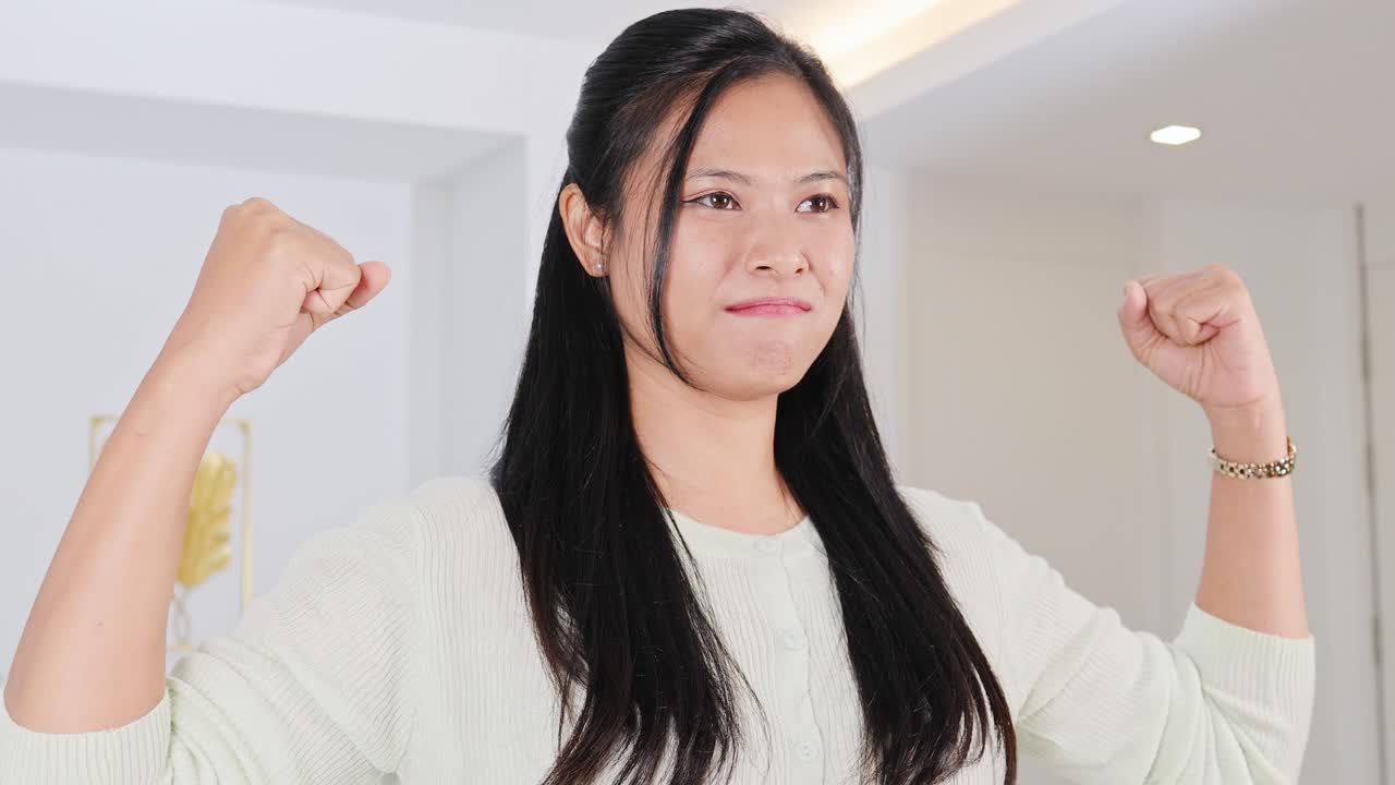 A woman confidently poses with flexed arms in a well-lit room, showcasing determination and empowerment