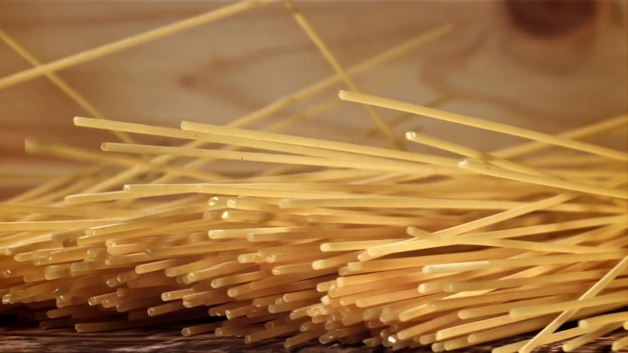 Spaghetti crudi che cadono su un tavolo di legno in movimento rallentato