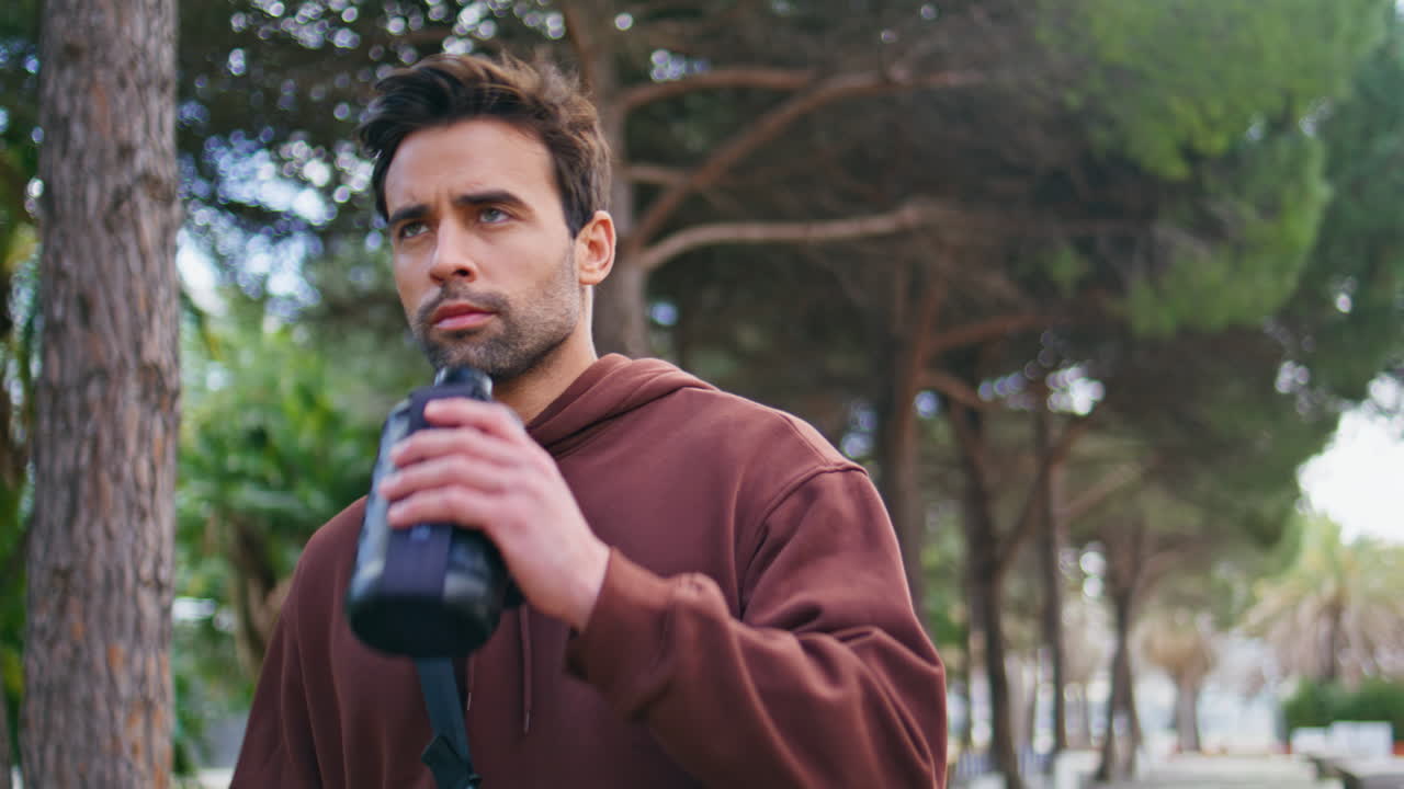 Athletic guy drinking water on street closeup. Handsome man runner hydrating