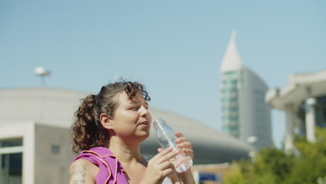 happy woman walking and drinking water after morning running