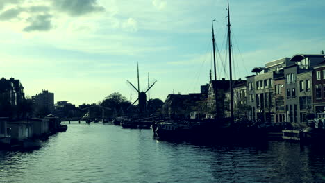 toma de lapso de tiempo del canal en leiden con barcos que pasan durante el día soleado y molino de viento en segundo plano