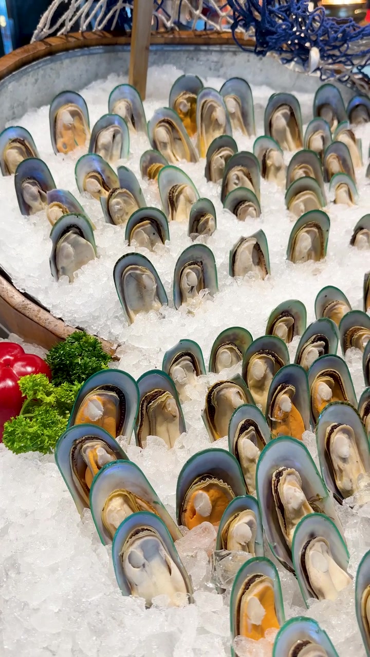 A person uses metal tongs to select fresh green lipped mussels from an ice display