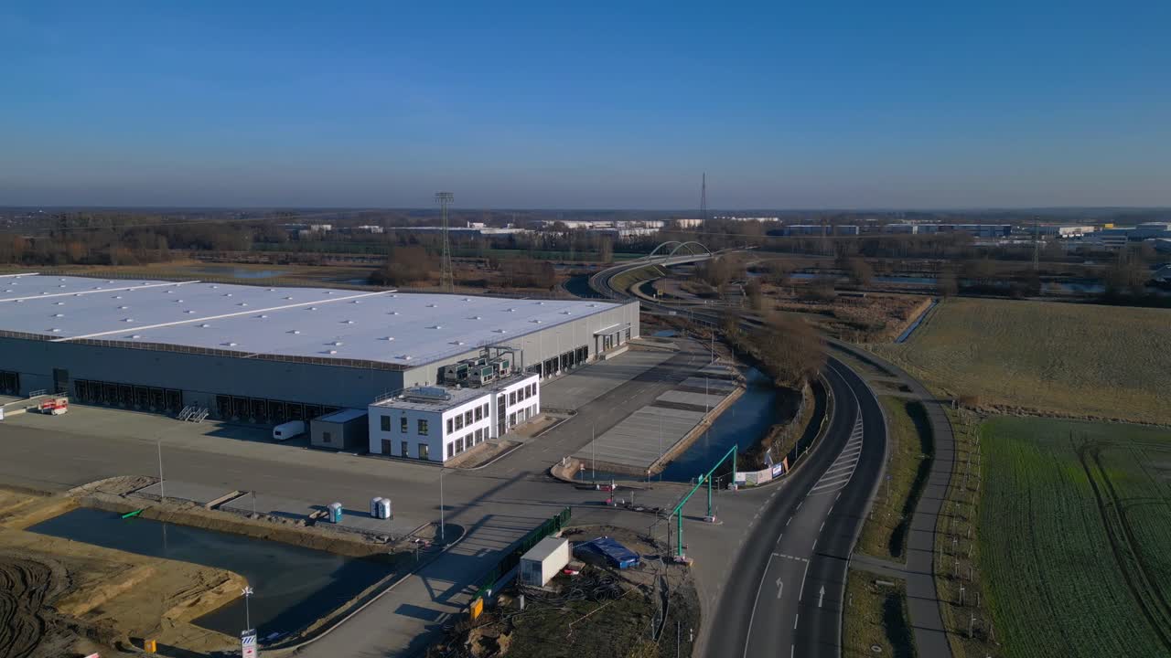Nuovo grande centro logistico in costruzione con una vasta area di stoccaggio, banchine di carico e terreno circostante vuoto. Splendida ripresa aerea con drone, rotazione panoramica verso sinistra