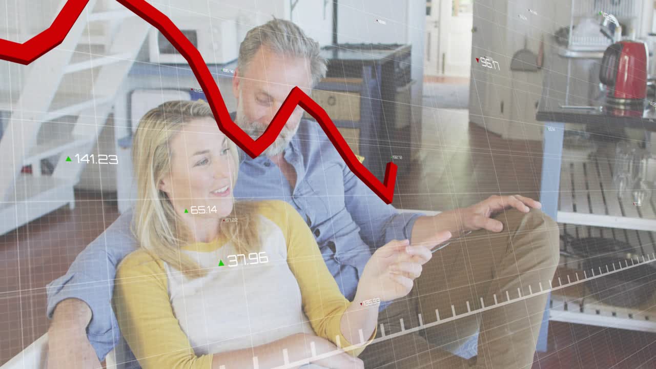 Casal se acomodando em sofá cinza, apontando para gráfico de linha vermelha variável sobreposto durante discussão financeira.