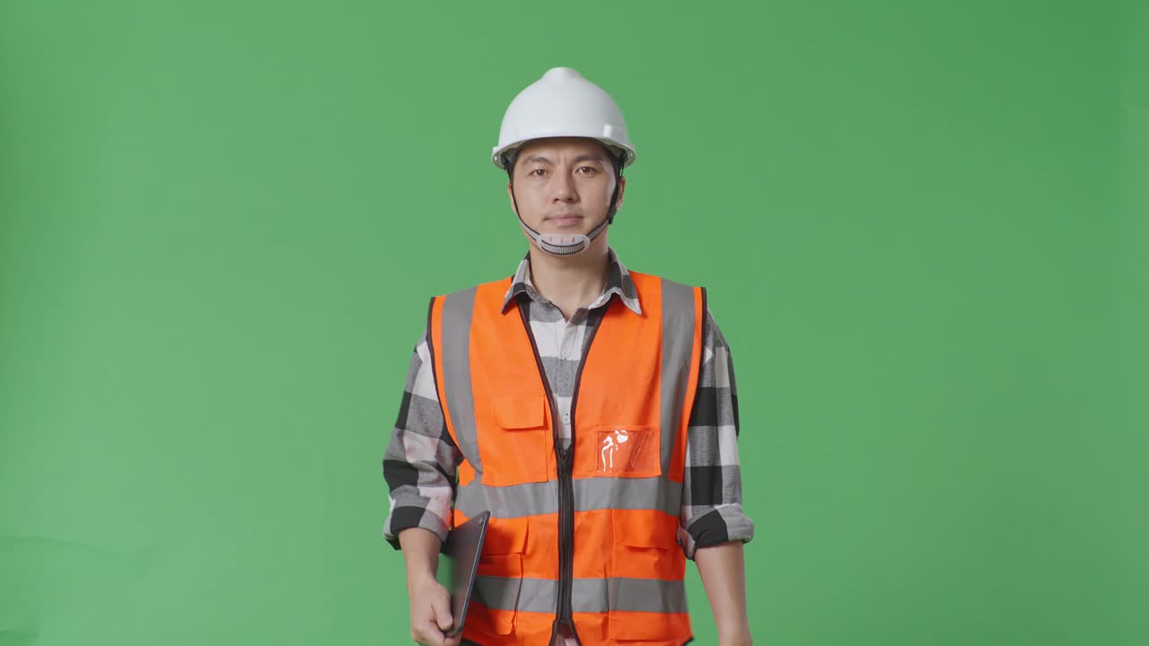 ingeniero masculino asiático con casco de seguridad sosteniendo una tableta mientras camina en el estudio de fondo de la pantalla verde