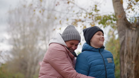 mother holds son affectionately as they smile during an autumn walk, with him holding a stick and playfully interacting with nature, creating a warm and joyful family bonding moment outdoors