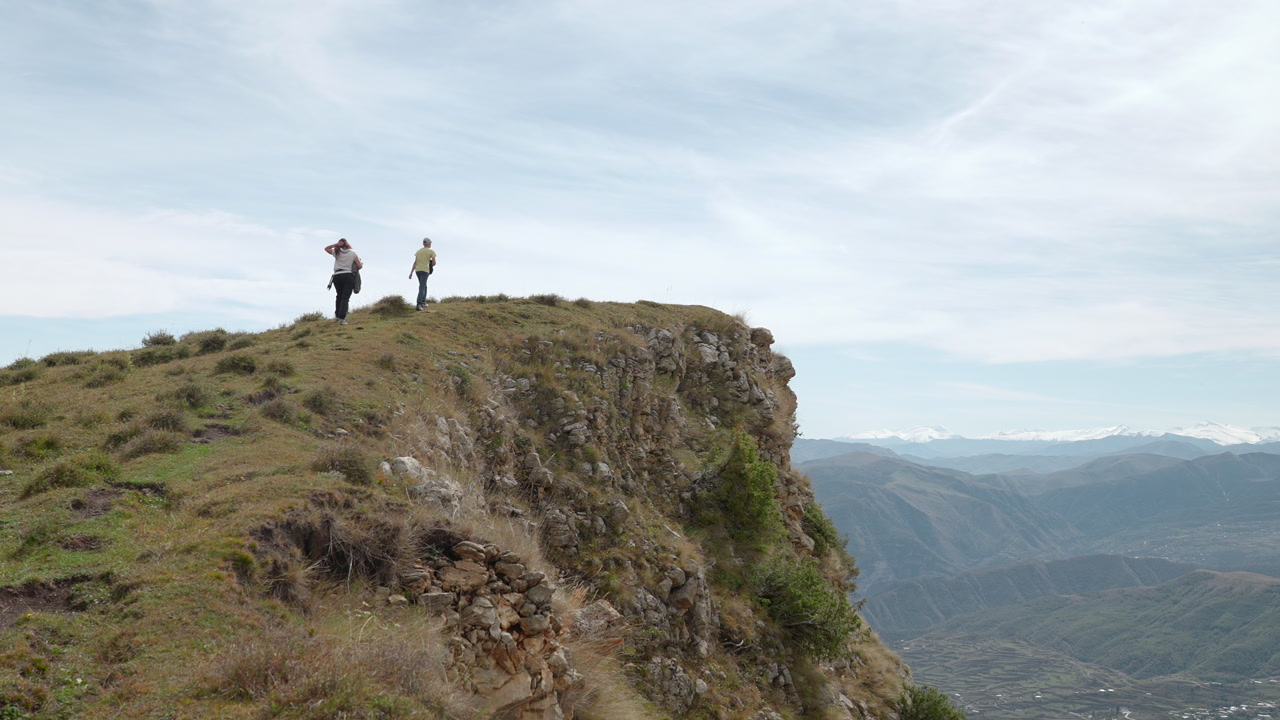 Lone Hiker Walking Toward Rocky Edge, Rear Perspective Shows Backpacked Trekker Ascending Ridge, Windblown. Creative