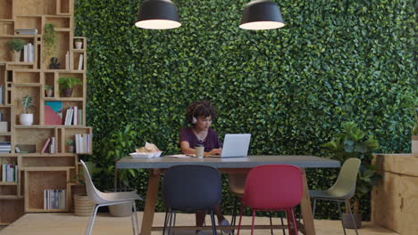 young black business woman working late using laptop computer brainstorming project drinking coffee in trendy startup office enjoying listening to music