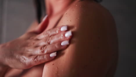 mujer extiende exfoliante en la piel en la unidad de ducha de cerca. dama hace rutina de cuidado de la piel usando producto cosmético orgánico en el baño. procedimiento de mimos corporal
