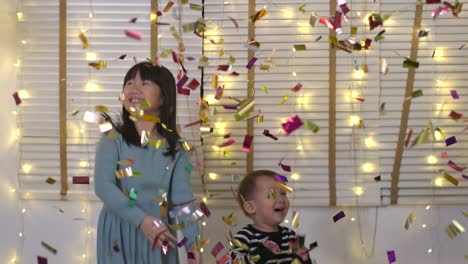 two happy asian children plays with confetti and have fun jumping in living room in slow motion.