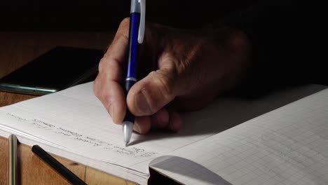 un hombre escribiendo en un bloc de notas con un bolígrafo, cerca de sus manos