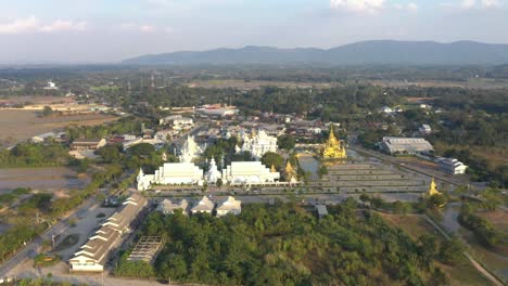 aerial drone of wat rong khun the huge buddhist white temple and golden temple with mountains and landscape in chiang rai, thailand