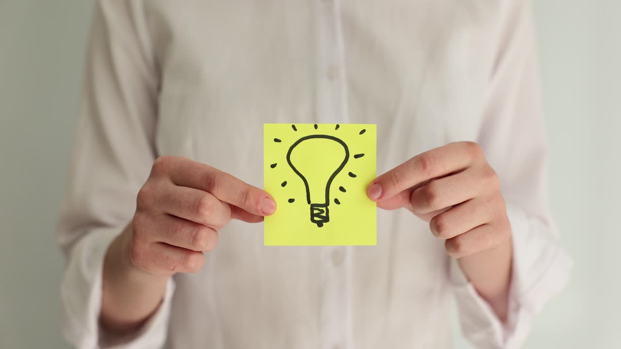 Person holding a yellow sticky note with a hand-drawn lightbulb, representing an idea or innovation