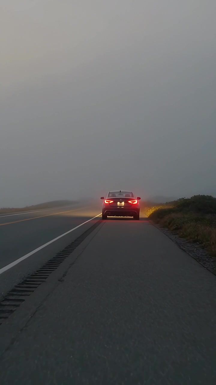 Vídeo vertical: Mostrando sedã escuro parado no acostamento nebuloso, luzes de freio iluminando através da neblina