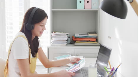 Mujer-Birracial-Feliz-Con-Auriculares-Teniendo-Videollamada-Con-Computadora-Portátil-En-El-Escritorio-Trabajando-En-Casa,-Cámara-Lenta