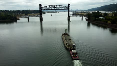 us, oregon, portland, st johns, 2025-07-26 - drone view of a barge being pushed by a tug on the willamette river under the raised railroad bridge