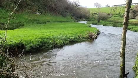 curving flooded river running through welsh valley farmland meadow slow motion