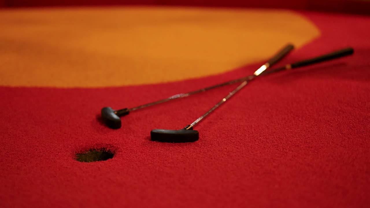 A red golf ball narrowly misses the hole on a vibrant red miniature golf course under warm lighting