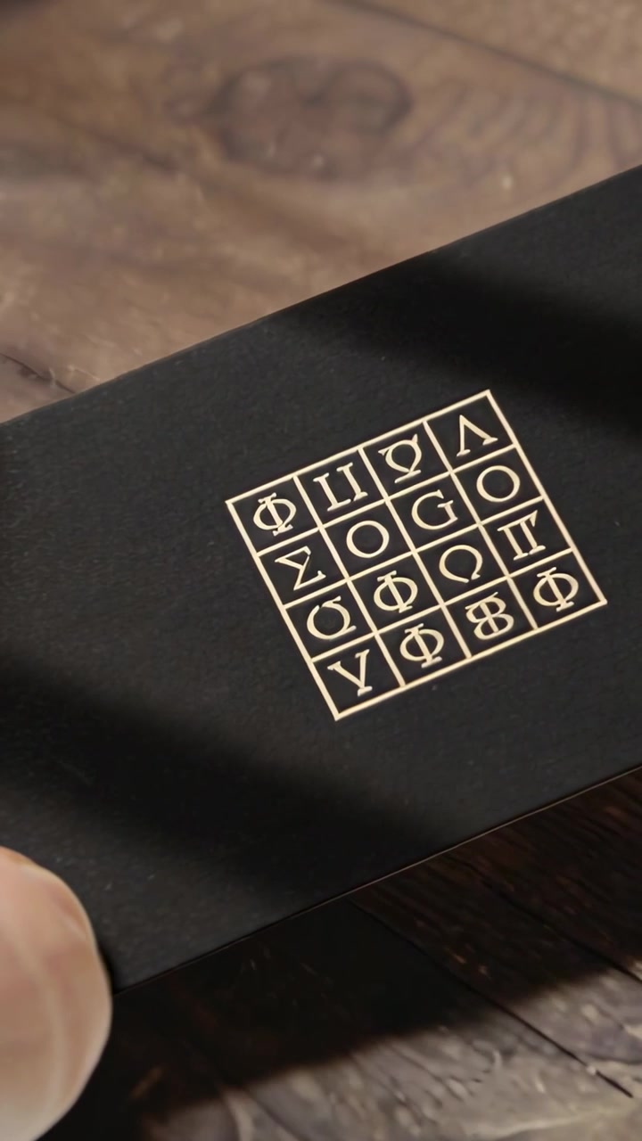 Video verticale: Pollice che spinge una scatola nera su un tavolo di legno, inclinando per ispezionare un emblema d'oro.